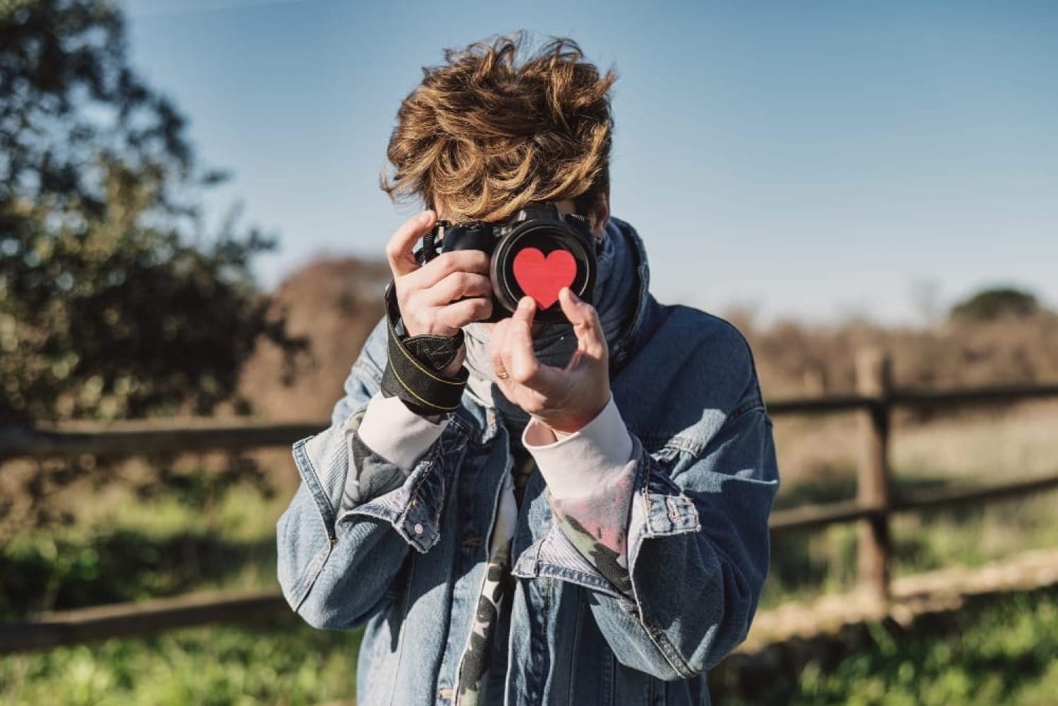 Photographer holding a red heart for Valentine's Day in front of his camera's lens